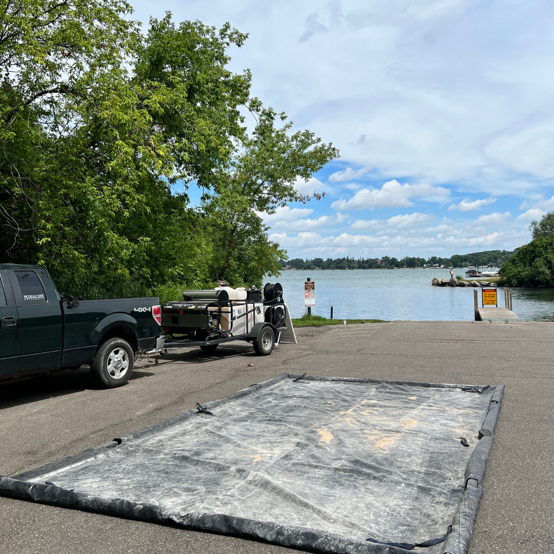 Black rectangular tarp utilized for mobile boat washing stations to catch contaminated water runoff. Black tarp is at boat launch in parking lot. 